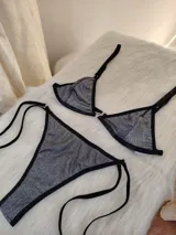 Conjunto de bikini de dos piezas en color plateado con acabado metálico y textura acanalada. El corpiño es de corte triangular con ribetes negros y una argolla central metálica. La bombacha es de corte colaless con tiras laterales ajustables y ribetes negros.