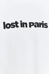 Remera oversize blanca de algodón con cuello redondo, mangas amplias por debajo del codo y estampado frontal con el texto "lost in Paris" en color negro.