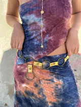 Cinturón de cuero sintético color dorado con textura, adornado con grandes aros metálicos de color bronce. El cierre es un gancho que se ajusta a los aros para regular el largo.