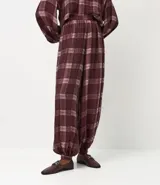 Pantalón estilo balloon de corte amplio y holgado, confeccionado en tejido de viscosa con estampado de cuadros en tonos bordó y blanco. Presenta cintura lisa y fruncido en los tobillos para un mayor volumen.