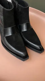 Botinetas de caña baja confeccionadas en una combinación de cuero napa y gamuza en tono bordó. Presentan un diseño de paneles con una banda central horizontal, puntera cuadrada y taco geométrico de color negro.
