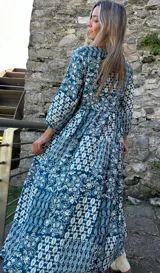 Vestido midi de corte holgado con estampado tipo paisley en tonos azul y blanco. Presenta mangas tres cuartos, escote redondo con pequeña abertura frontal y cordón ajustable en la cintura con borlas decorativas.