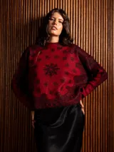 Buzo de punto de manga larga con cuello redondo, confeccionado en un tejido suave de textura peluda. Presenta un diseño estampado con motivos florales y ornamentales en color negro sobre una base de color rojo intenso.