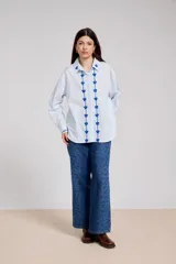 Camisa blanca de corte holgado con cuello camisero y cierre frontal de botones. Presenta un delicado bordado vertical de flores pequeñas en color bordó a lo largo de la botonera y en el cuello.
