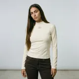 Polera de manga larga en color crudo con cuello alto y detalle de costuras curvas en el frente, además de un sutil bordado en el pecho.