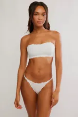 Tanga de microfibra color blanco, con tiro bajo, tiras finas y bordes con terminación de puntilla festoneada.
