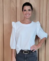 Blusa blanca de algodón tussor, con cuello redondo, mangas 3/4 abullonadas y detalle de volados en los hombros.