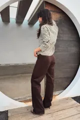 Pantalón de tiro alto confeccionado en tejido con efecto ante, de corte recto y diseño minimalista con trabillas en la cintura y cierre frontal con cremallera y gancho metálico.