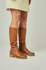 Bota de caña media alta confeccionada en cuero vacuno engrasado, con cierre lateral y suela con vira. Presenta un diseño clásico con taco bajo.