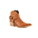 Bota texana de caña baja en cuero color suela, con taco cuadrado de madera y punta fina. Presenta una correa con estribo metálico decorativo alrededor del tobillo y costuras decorativas en la puntera.