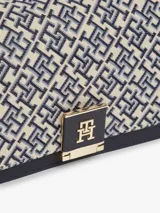 Cartera bandolera Tommy Hilfiger de diseño estructurado, confeccionada en jacquard con monogramas TH en tonos azul marino y beige, combinada con detalles en cuero sintético negro. Cuenta con solapa frontal, cierre metálico con logo, asa superior y correa extraíble.