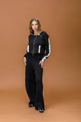 Conjunto de dos piezas compuesto por una campera con capucha y cierre frontal, y un pantalón de corte recto. Ambas prendas son de color negro con bandas laterales blancas y detalles en blanco en los bolsillos de la campera.