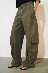 Jeans cargo de tiro medio y corte barrel leg, color verde militar. Presenta bolsillos laterales con solapa en las piernas, bajo ajustable con trabilla y botón, y cierre frontal con cremallera y botón.