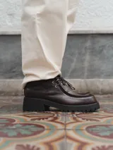 Zapato de cuero negro con cordones, detalle de pespuntes en la puntera y suela de goma con plataforma.