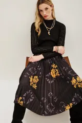 Falda midi plisada de color negro con estampado floral en tonos amarillos y detalles de efecto tie-dye. Presenta una silueta acampanada con movimiento y cintura elástica.