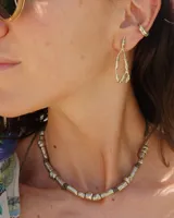 Collar artesanal compuesto por piezas metálicas irregulares con acabado dorado, ensartadas en un cordón de hilo de algodón natural. Presenta un sistema de nudo corredizo para ajustar el largo.