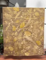 Mantel rectangular grande de algodón con estampado botánico en tonos dorados sobre fondo marrón.