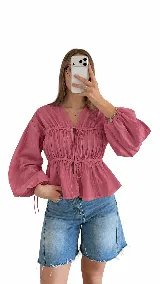 Blusa blanca de manga larga amplia, con escote en V y frunces en el cuerpo. Posee cordones ajustables con lazos en el frente y en la cintura.