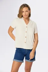 Camisa lisa de lino color beige, de manga corta, con cuello camisero, bolsillo ojal en el pecho y cierre frontal con botones.