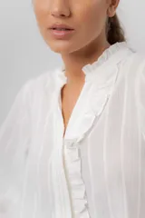 Camisa de manga larga color beige con diseño a rayas sutiles, cuello mao con volados y abertura frontal con detalles de volados a un lado.