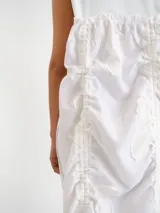 Vestido midi blanco sin mangas, con cuello redondo y diseño holgado. Presenta un cordón ajustable fruncido en el centro de la parte frontal y parches circulares sutiles en la tela.