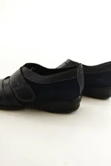 Zapato de cuero negro con cierre de velcro ancho y costuras pespunteadas a contratono.