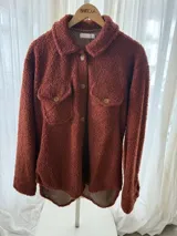 Campera de corderito color terracota, con cuello camisero, cierre frontal de botones, bolsillos con solapa en el pecho y forro interior estampado.