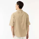 Camisa de manga corta de popelín color beige, con cuello clásico y cierre frontal de botones.