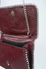 Cartera de hombro con solapa y bordes ribeteados con una cadena metálica entrelazada. Presenta un diseño tipo sobre con acabado texturizado y una correa de cadena larga.