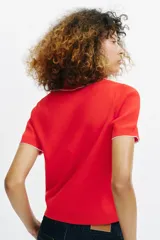 Top de punto color crudo, con cuello polo y escote en V. Cuenta con mangas cortas y detalle de puntilla con forma de onda en el cuello y los puños.