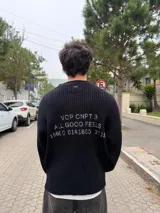 Sweater de punto acanalado color negro, con cuello redondo y calce relajado. Presenta un estampado tipográfico en la espalda con el texto 'VCP CNPT. ALL GOOD FEELS' y números en color gris.
