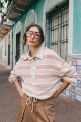 Remera tipo polo de tejido de punto a rayas horizontales en tonos rosados y beige. Presenta cuello camisero de lino, cierre frontal con botones de nácar y silueta holgada.