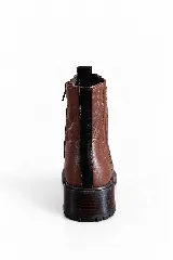Botin de cuero vacuno color marrón, con taco bajo y suela track. Presenta una franja vertical negra en la parte trasera y cierre lateral.