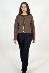 Cardigan de punto color marrón chocolate, con cuello redondo y cierre frontal de botones decorados con lentejuelas circulares brillantes. Presenta mangas largas y un corte recto.