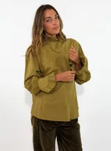 Camisa de algodón color verde oliva, con cuello alto con volados, cierre frontal oculto y mangas largas con puños con volados.