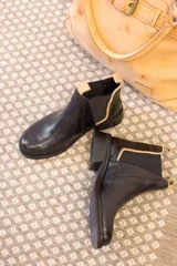 Botas tipo Chelsea de cuero negro, con paneles laterales elásticos y detalle de textura grabada en el talón. Presentan un borde en color beige y tiradores en la parte superior.