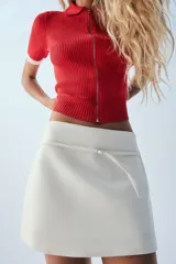 Falda pantalón de tiro medio, color crudo, con detalle de cinturón fino con hebilla metálica y cierre lateral con cremallera oculta.