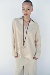 Blusa amplia confeccionada en mezcla de viscosa y lino, color beige, con cuello solapa, escote en V y manga larga.