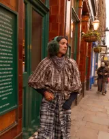 Camisa de manga larga con estampado a cuadros en tonos beige, marrón y azul. Presenta volados en las mangas, botones a la vista, puños elásticos y tiritas ajustables en el dobladillo para entallar.