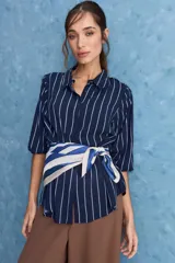 Camisa de calce relajado con cuello clásico, mangas largas con puños elastizados y rayas verticales que aportan un estilo atemporal. Su diseño liviano y versátil cuenta con estampado floral verde sobre fondo de rayas celestes y blancas.