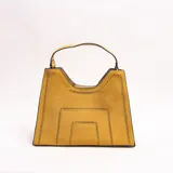 Cartera tipo tote de eco-cuero gamuzado color mostaza, con diseño estructurado de base trapezoidal y detalles calados geométricos. Cuenta con asa superior corta.