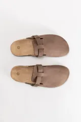 Zueco de gamuza color marrón con tira ajustable y hebilla metálica. Presenta una plantilla de corcho y suela de goma negra.