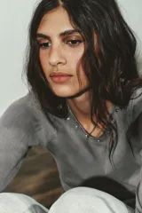 Camiseta de manga larga color gris con efecto lavado, cuello redondo y bajo redondeado. Presenta aplicaciones de tachas metálicas alrededor del escote y en el bajo.