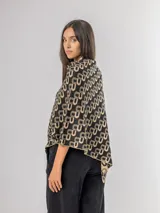 Poncho liviano con diseño geométrico de letras entrelazadas en color negro y beige. Presenta un corte asimétrico y caída fluida, ideal para superponer sobre otras prendas.