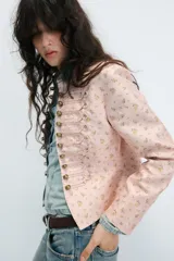 Blazer entallada de cuello alto y manga larga, en color rosado con estampado de flores amarillas. Cuenta con detalle de pasamanería en el delantero y cierre frontal con botones metálicos dorados.