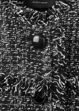 Chaqueta de tweed en tejido jaspeado negro y blanco, con diseño recto, cuello redondo, manga larga y cierre delantero con botones. Presenta terminaciones deshilachadas y detalles de flecos.