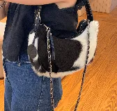 Cartera tipo shoulder bag de cuero con pelo vacuno en estampado animal print blanco y negro. Cuenta con manija corta de cuero con tachas y correa larga desmontable de cadena metálica entrelazada con tira de cuero. Incluye cierre superior y detalle de llavero redondo colgante con logo grabado.