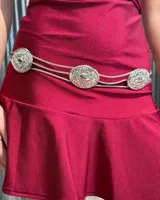 Cinturón tipo caderín compuesto por tres cadenas finas entrelazadas y tres apliques circulares metálicos con diseño labrado y centro liso.