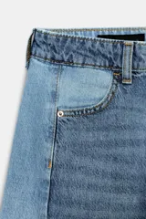 Jeans de tiro medio con diseño barrel y paneles laterales en un tono de denim más claro que contrasta con el centro. Presenta cinco bolsillos, cierre frontal con cremallera y botón, y bajo con acabado sin costura.
