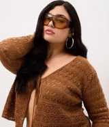 Saco corto de tricot marrón con diseño de puntos calados, escote en V, mangas largas y cierre frontal con lazo ajustable.